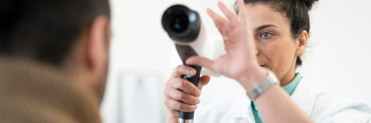 Doctor lifting Aurora IQ handheld fundus camera near patients eye